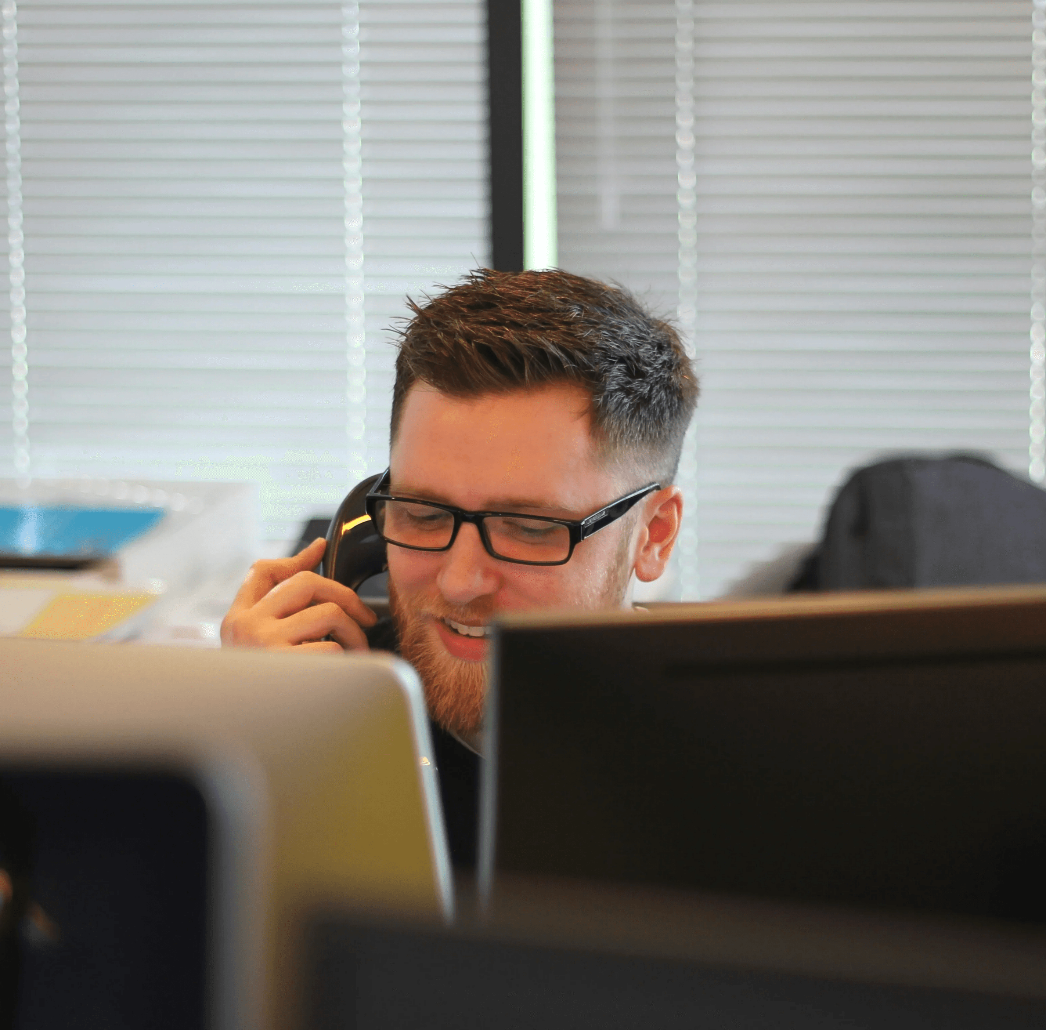 A man in an office setting on the phone while monitoring alarms installed by Axe Fire & Security, symbolizing 24/7 alertness.