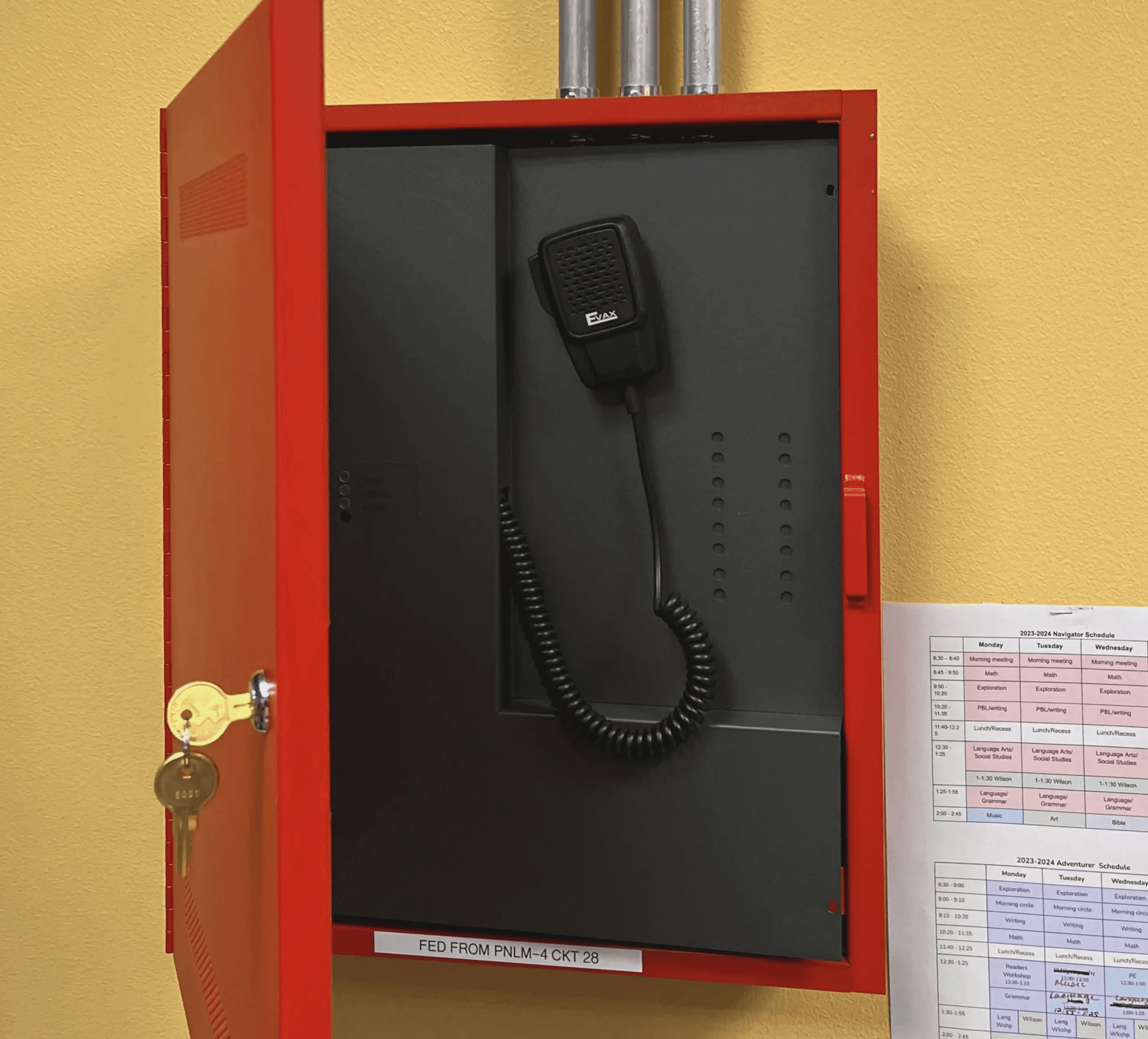 Red emergency phone box mounted on a wall with conduit pipes above, part of a fire alarm system inspected and serviced by Axe Fire & Security, showcasing readiness for emergency communication.
